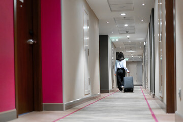 A girl with a suitcase walks down the hotel corridor rear view of a business woman during a trip