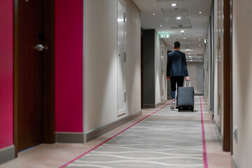 A man with a suitcase walks down the hotel corridor a back view of a businessman on a trip