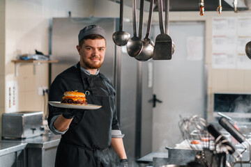 professional kitchen in a hotel restaurant, a satisfied chef shows a freshly prepared burger on a...