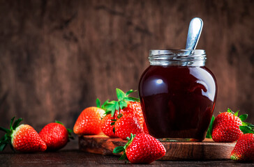 Strawberry jam in glass jar and fresh berries, rustic wooden table background, copy space
