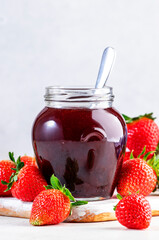 Strawberry jam in glass jar and fresh berries, white table background, copy space
