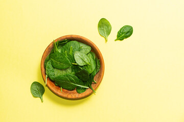 Fresh juicy baby spinach leaves in the wooden bowl on light yellow background top view. Healthy tasty food concept.
