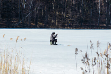 Fisherman fishing on a frozen lake in the early spring with fishing pole, ice auger and equipment...
