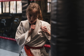 A girl in a kimono exercises with a punching bag in the gym while learning karate martial arts © Guys Who Shoot