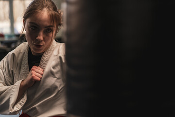 A girl in a kimono exercises with a punching bag in the gym while learning karate martial arts