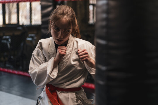 A girl in a kimono exercises with a punching bag in the gym while learning karate martial arts - Powered by Adobe