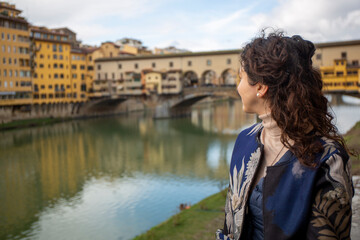 Fototapeta na wymiar Woman looks at the Ponte Vecchio on the Arno river in the middle of the city of Florence with a sky with clouds, Italy