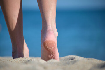 Fototapeta na wymiar Close up of female feet walking barefoot on white grainy sand of golden beach on blue ocean water background