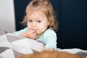 thoughtfulness toddler girl puts finger in mouth, authentic thinking - obrazy, fototapety, plakaty