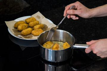 Bolinhos de bacalhau, very famous in Portuguese gastronomy. Fried dumpling, cod dumpling, fish, salted cod fritters, bacalao bunuelos. Person in the kitchen frying cod fritters. Preparation mode.