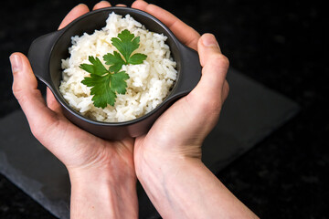 Dry white rice, as an accompaniment to various dishes. Hands holding pot with rice.