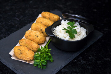 Bolinhos de bacalhau, very famous in Portuguese gastronomy. Fried dumpling, cod dumpling, fish, salted cod fritters, bacalao bunuelos. Codfish cake served with white rice on a dark background.