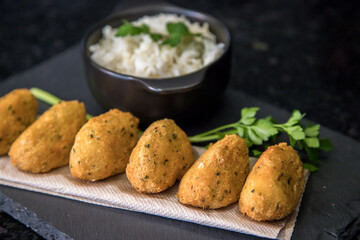 Bolinhos de bacalhau, very famous in Portuguese gastronomy. Fried dumpling, cod dumpling, fish, salted cod fritters, bacalao bunuelos. Codfish cake served with white rice on a dark background.