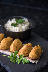Bolinhos de bacalhau, very famous in Portuguese gastronomy. Fried dumpling, cod dumpling, fish, salted cod fritters, bacalao bunuelos. Codfish cake served with white rice on a dark background.