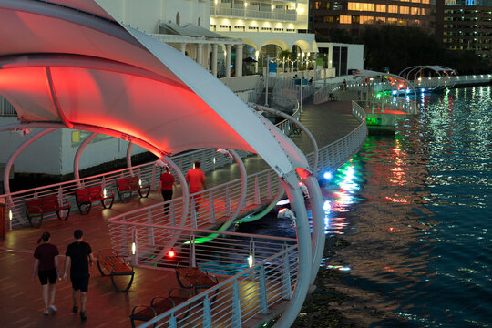 People enjoying time walking on pedestrian riverwalk trail alongside river water in downtown district of Tampa city in Florida, USA. Recreational area in modern american megapolis