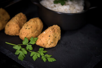 Bolinhos de bacalhau, very famous in Portuguese gastronomy. Fried dumpling, cod dumpling, fish, salted cod fritters, bacalao bunuelos. Codfish cake served with white rice on a dark background.