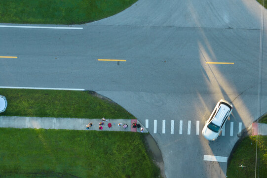 Top view of schoolkids waiting for school bus to arrive in time. Kids standing on suburban street sidewalk ready to be picked up in early morning. Public transportation in the USA - Powered by Adobe