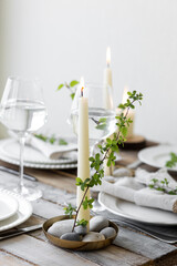 Rustic zero waste wedding decor with natural elements. Wooden table, candles, linen napkins, branches with green leaves. Eco-friendly decoration for the special holiday dinner. Romantic and cozy place