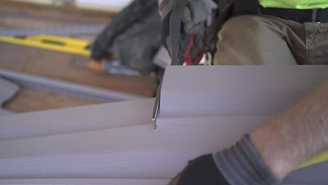 Finishing the house with siding: preparatory work. A man cuts gray siding with construction scissors.