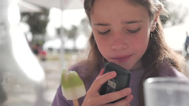 Young girl seated outdoors eating an ice cream and checking her blood sugar level	
