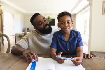 Obraz premium Happy african american father and son sitting at table with notebook and having video call
