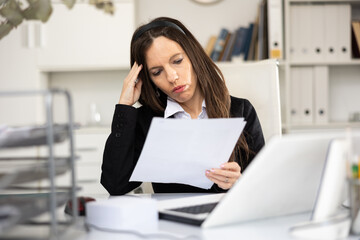 Portrait of tired woman office worker sitting at table and doing paperwork during her workday.