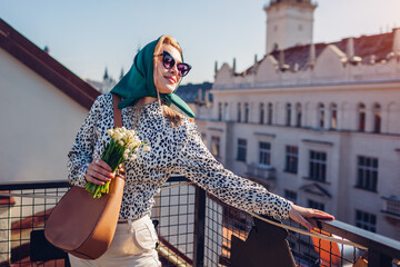 Stylish happy woman wearing green retro shawl with sunglasses holding spring flowers. Classic vintage outdoor fashion