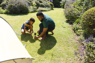Happy african american father and son pitching tent in garden