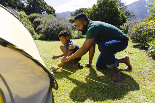 Happy african american father and son pitching tent in garden - Powered by Adobe