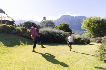 Happy african american father and son playing football in garden