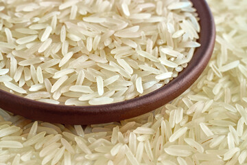 Healthy basmati rice in a clay ceramic bowl close-up against the background of scattered grains of rice