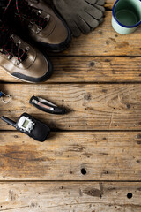 Camping equipment of trekking shoes, metal cup, walkie talkie on wooden background with copy space