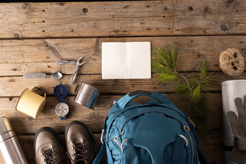 Camping equipment of backpack, metal cup and blank notebook on wooden background with copy space