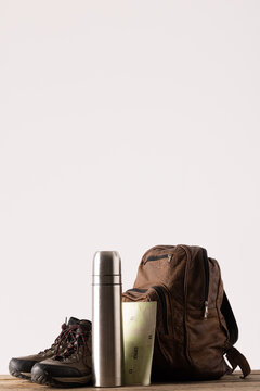 Close up of backpack, trekking shoes and thermos on table on white background with copy space