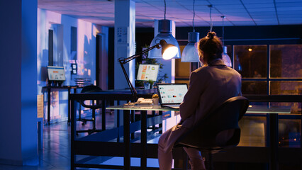 Executive manager working on financial development late at night, sitting at business office desk to plan investment. Young woman analyzing economy graphs and analytics. Handheld shot.