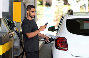 Serious man refueling his luxury car and messaging smartphone at the gas station. Iranian guy pouring petrol into tank of modern vehicle on filling station in city  