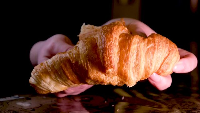 female hands break fresh warm croissant delicious breakfast homemade cakes on a black background crumbs falling on a stone table are visible light structure porous pastries bread dessert
