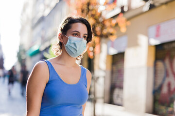 young hispanic woman walk in the city shopping. urban casual with face mask.