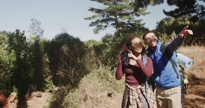 Happy african american couple hiking and wearing backpacks, taking pictures in forest, slow motion