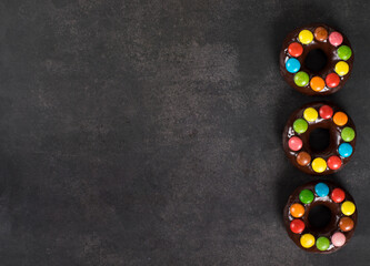 Chocolate donuts with chocolate glaze and decorated with colorful dragees. Dark gray background....