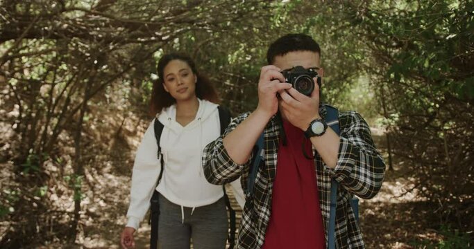 Happy african american couple wearing backpack, hiking and taking pictures in forest, slow motion