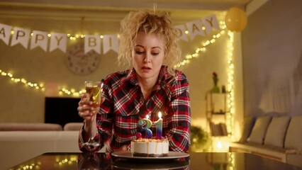 A sad woman picking up a champagne glass and taking a small sip out of it. Candles on a birthdayt cake create a number 31. She looks troubled possibly by her growing old. High quality 4k footage
