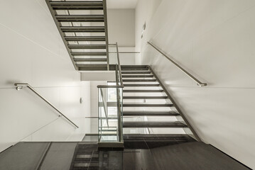 Lightly designed stairs made of stainless steel, tempered glass and polished black granite steps in an office building