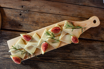 Serving board with slices of hard goat cheese garnished with sweet ripe figs and fragrant rosemary...