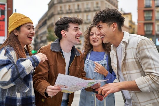 A group of diverse friends enjoying their Spain vacation, happily selecting destinations on a city map with laughter.