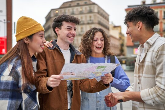 A diverse group of friends laughing and planning their Madrid sightseeing adventure with a city map in hand.