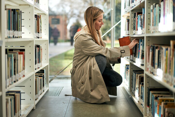 Curious young student looking for a book on a library on a sunny spring day