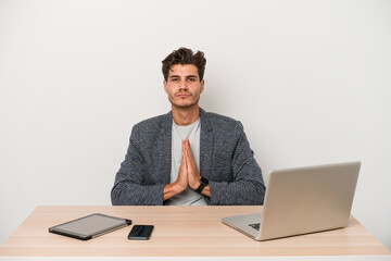 Young entrepreneur man working with a laptop isolated praying, showing devotion, religious person looking for divine inspiration.