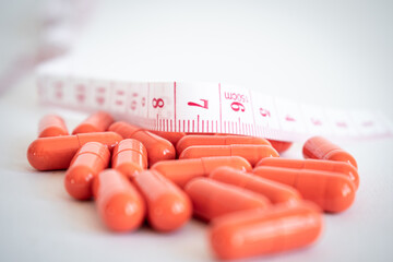 close-up shot of a pile of orange pills and a white tape measure with red numbers. White background. concept of dependence on weight loss pills.