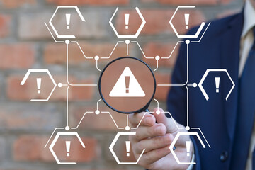 Businessman holding magnifying glass and working on virtual touchscreen of future sees icon: attention sign. Notification error and maintenance business technology concept.